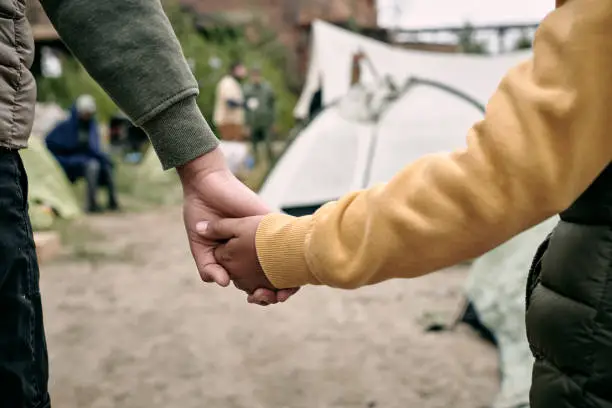 Rear view of unrecognizable children of different ages holding hands while coming in to migrant camp