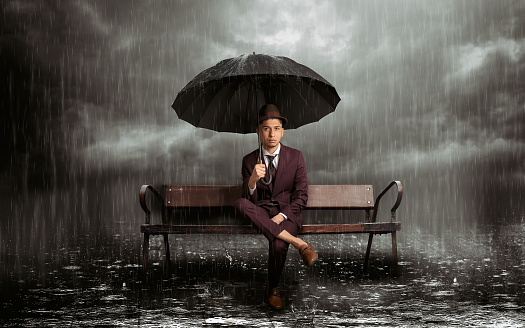 Latin man sitting on a bench with umbrella in the rain in the middle of a stormy night, horizontal