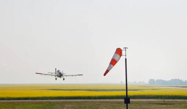 Crop Duster flies low over canola field, with wind sock in the foreground