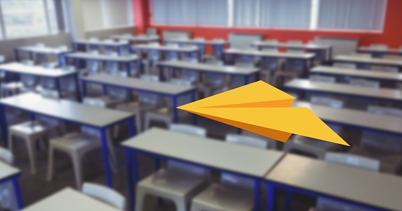 Composition of yellow paper aeroplane flying over desks in empty classroom. school, education and study concept digitally generated image.