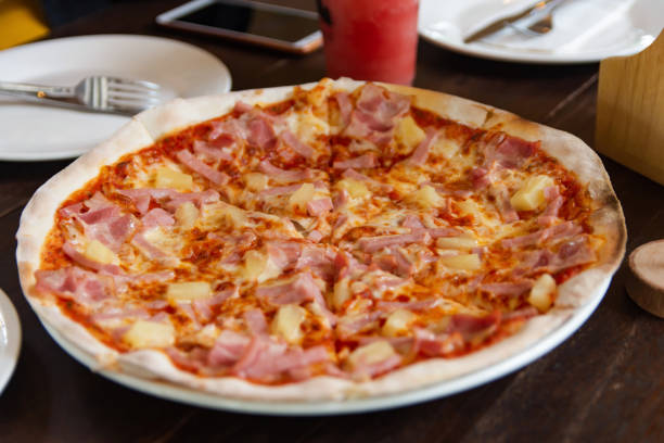 istock hawaiian pizza with ham, pepperoni, tomatoes on wooden table 1340760137