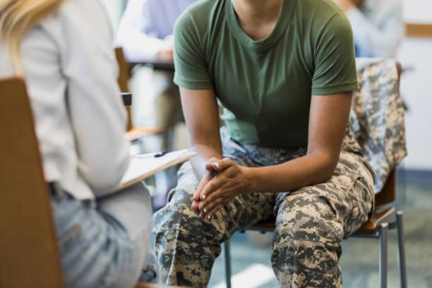 Close up photo female soldier leaning forward in seat A close up photo of an unrecognizable mid adult female soldier as she puts her hands together and leans forward in her seat.  She is talking with an unrecognizable female counselor. war veteran stock pictures, royalty-free photos & images