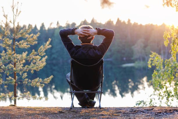 ein mann sitzt bei sonnenuntergang im freien in einem klappstuhl. - campingstuhl stock-fotos und bilder