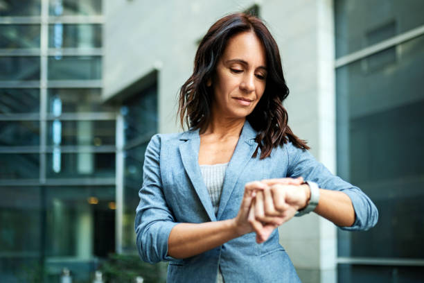 joven mujer de negocios seria y exitosa mirando su reloj de pulsera fuera del edificio de oficinas - impaciencia fotografías e imágenes de stock