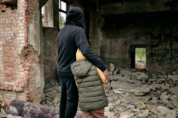 Looking At Ruins Of House Rear view of father embracing child and looking at ruins of house after hostilities refugee photos stock pictures, royalty-free photos & images