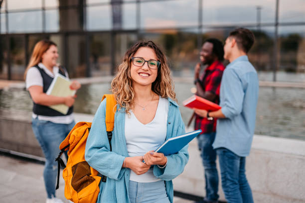 Beautiful smiling female college student Portrait of a smiling female university student standing on campus with friends in the background. student stock pictures, royalty-free photos & images