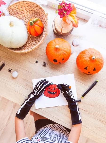 istock A child in black gloves draws a laughing pumpkin while sitting by the window. 1340773966