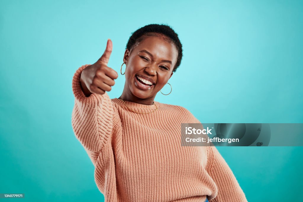 Shot of a beautiful young woman showing thumbs up while standing against a turquoise background We need more good vibes Thumbs Up Stock Photo