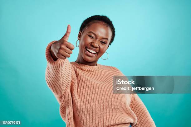 Shot Of A Beautiful Young Woman Showing Thumbs Up While Standing Against A Turquoise Background Stock Photo - Download Image Now