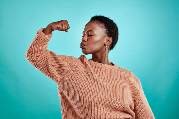 foto de una hermosa joven flexionándose mientras está de pie sobre un fondo turquesa - flexing muscles fotos fotografías e imágenes de stock