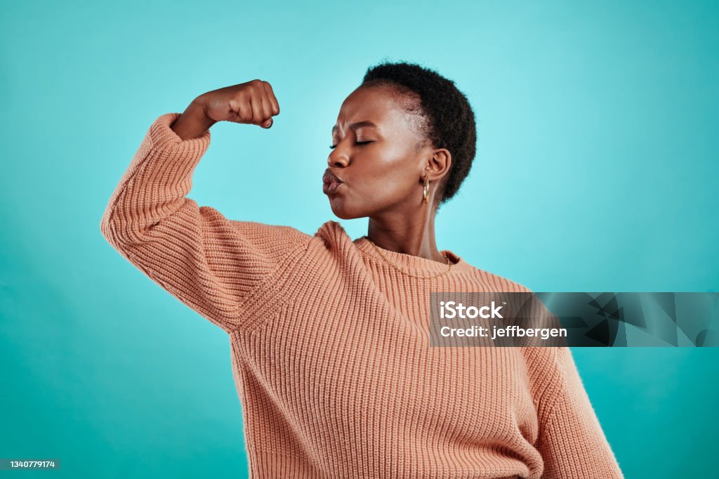 Shot of a beautiful young woman flexing while standing against a turquoise background We can do just about anything we put our minds to Confidence Stock Photo