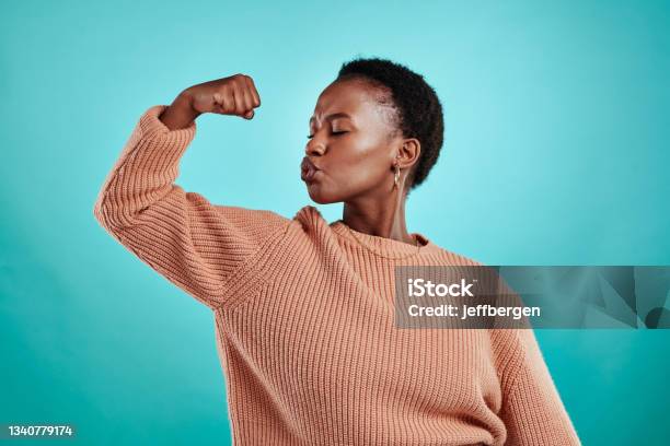Shot Of A Beautiful Young Woman Flexing While Standing Against A Turquoise Background Stock Photo - Download Image Now