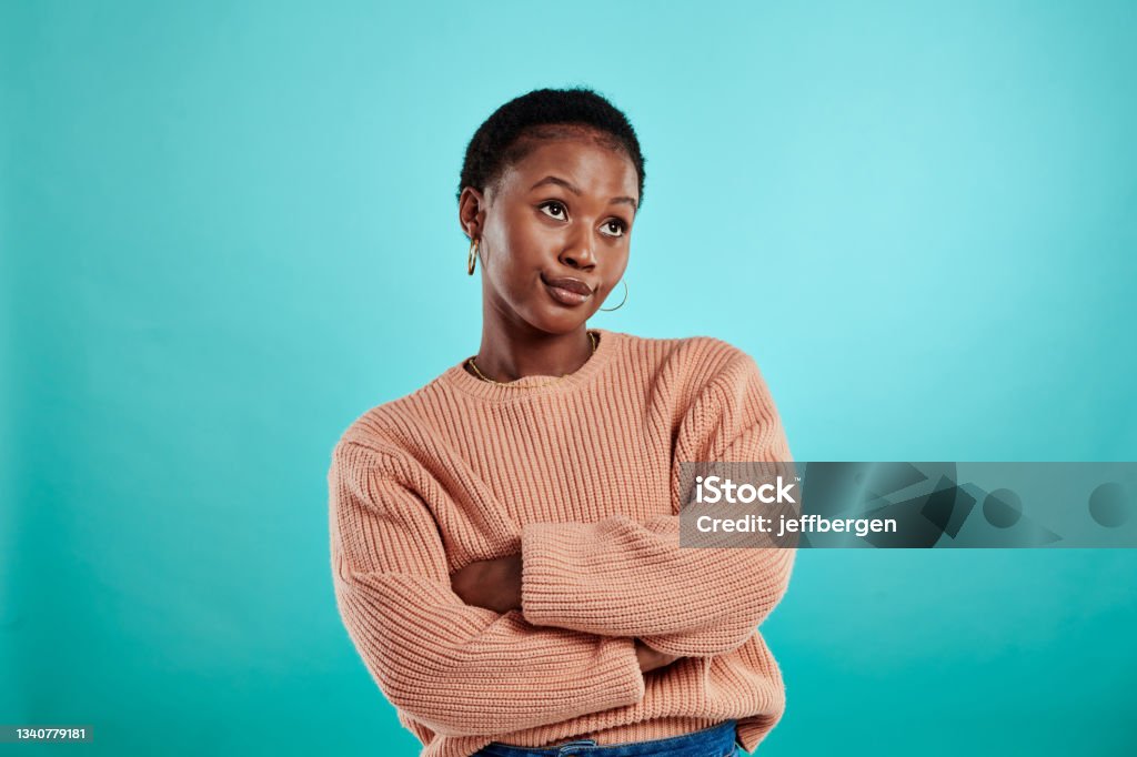 Shot of a woman standing with her arms crossed against a turquoise background My attitude depends on you Displeased Stock Photo