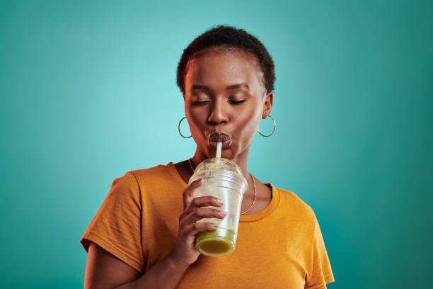 scatto di una giovane donna che beve un succo verde mentre si trova su uno sfondo turchese - smoothie drinking women drink foto e immagini stock