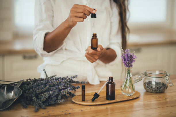 mujer joven aplicando aceite esencial orgánico natural en el cabello y la piel. spa casero y rituales de belleza. - aromatic oil fotografías e imágenes de stock