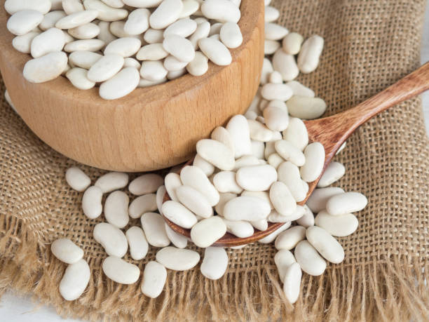 istock white beans in a wooden spoon on a white wooden table, copy space 1340786158