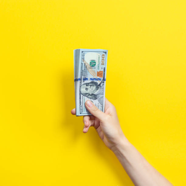 istock Hand holding a big stack of banknotes isolated on yellow background. Wealth or loan concept 1340786321