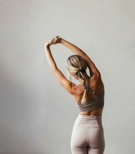 A young blonde Caucasian woman stretching A portrait of a young blonde Caucasian woman stretching her back from behind cooling down stock pictures, royalty-free photos & images