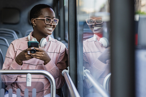 Woman is sitting in the bus, holding smart phone and looking through the window