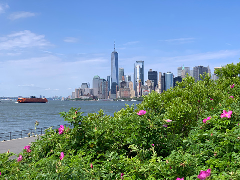 Downtown Manhattan with Staten Island ferry behind the green of Governor Island on a sunny day