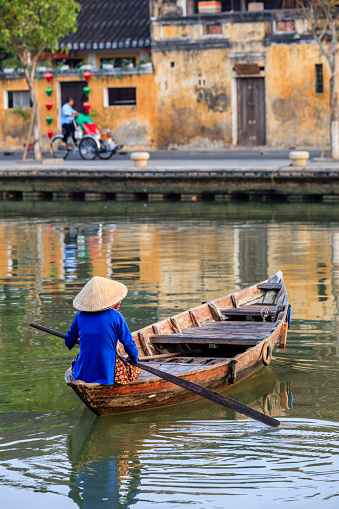 Vietnamese woman in a row boat, old town in Hoi An city, Vietnam. Hoi An is situated on the east coast of Vietnam. Its old town is a UNESCO World Heritage Site because of its historical buildings.
