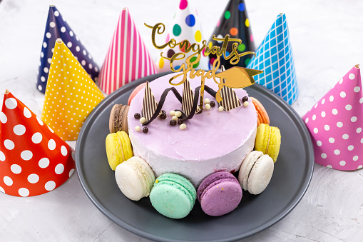 Violet birthday cake with topper Congrats grad, paper hats, macaroons on a table. Decoration for graduation party