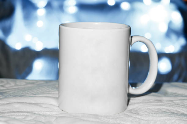 white mug on the bed, mug on white cloth, space for advertising text, blue background. defocused lights background. advertising concept. sublimation