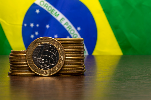 stack of Brazilian coins with a real highlighted and the Brazilian flag in the background. selective focus.