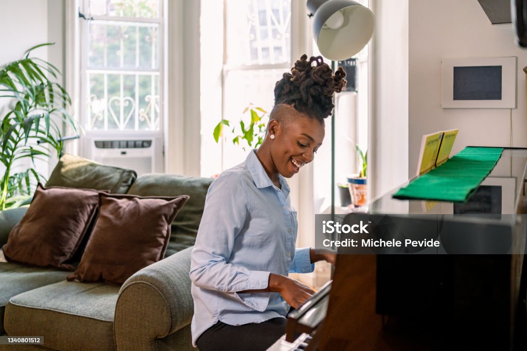 Black woman playing piano at home Adult Stock Photo