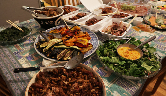A summer potluck dinner includes grilled vegetables, salad, barbecued meat and prepared platters. Family home in Toronto.