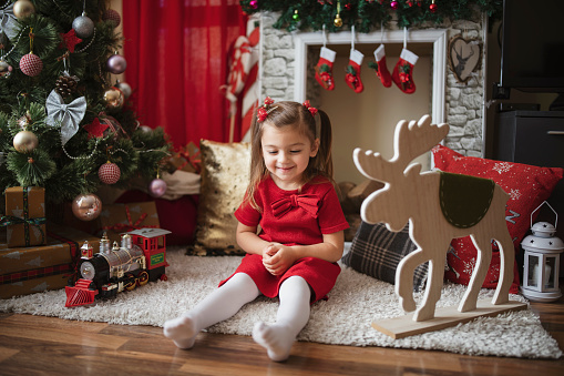 Cute girl sitting on the carpet around Christmas decoration at home