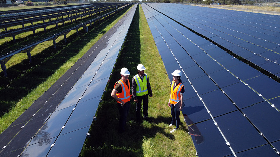 Three Engineers Surrounded By Solar Panels On Solar Farm in Australia. Shot from Drone.