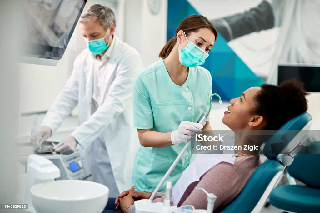 African American woman having dental treatment at dentist's office. Young dental nurse performing dental procedure on black female patient before teeth examination at dentist's office. Dentist Stock Photo