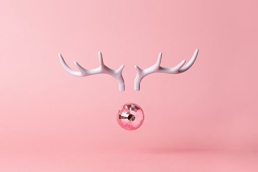 Christmas reindeer concept on pink background made horns and Xmas party ball on pastel pink background. Minimal winter vacation idea.