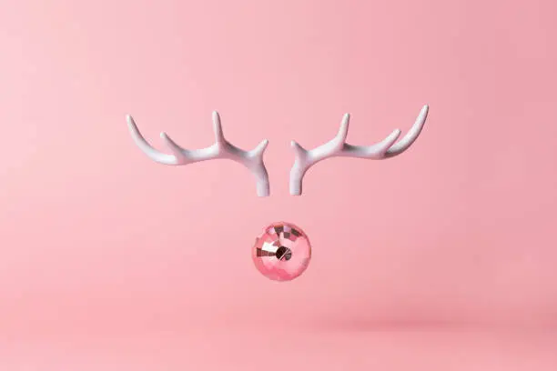 Photo of Christmas reindeer concept on pink background made horns and Xmas party ball on pastel pink background. Minimal winter vacation idea.