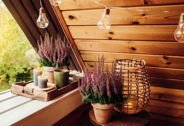 Photo of Small natural color wooden cabin balcony with heather flowers, candlelight flame and steaming cup of tea coffee. Cute autumn hygge home decor arrangement.