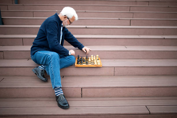 Good looking senior man playing chess with himself. He is sitting on stairs of riverside waterfront