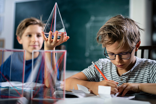 Little boys in school classroom learning the geometry.\nKids are using 3D models of polyhedrons as teaching aids.\nNikon D850