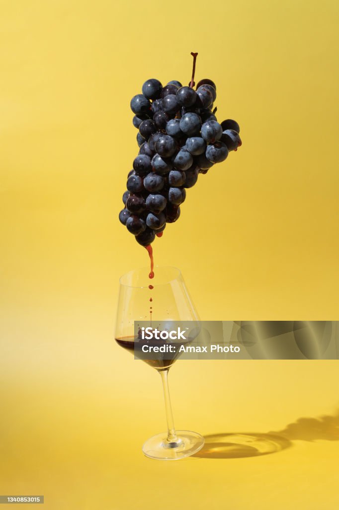 Still life with black grapes and flowing red wine into a glass on yellow background Wine Stock Photo