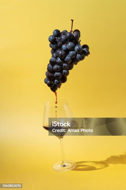 Still Life With Black Grapes And Flowing Red Wine Into A Glass On Yellow Background Stock Photo - Download Image Now