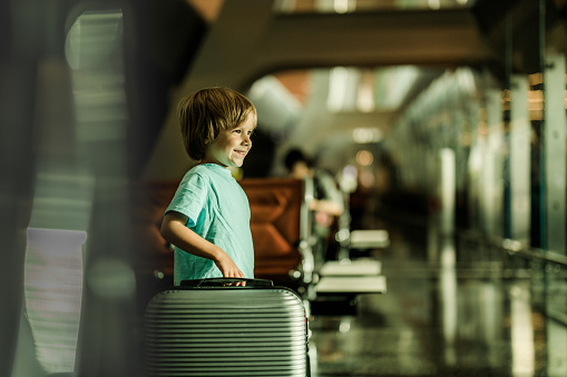 Happy little boy with travel bag at airport's waiting room.