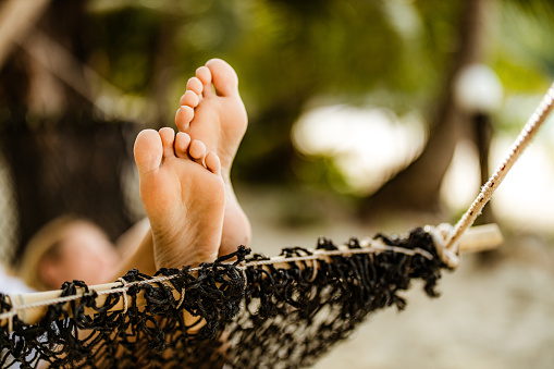 Close up of barefoot woman relaxing in hammock during summer vacation on the beach.