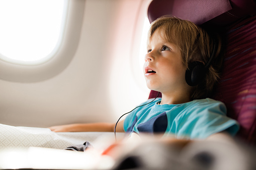 Cute boy traveling by plane and listening something over the headphones.
