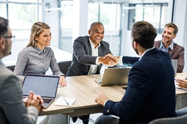 Happy businessmen shaking hands on a meeting in the office. Happy male entrepreneurs came to an agreement during a meeting with their colleagues in the office. Focus is on black man. businesswear stock pictures, royalty-free photos & images