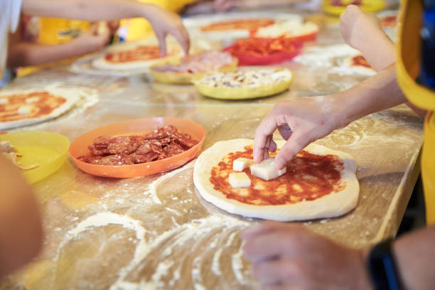 Pizza Workshop for children Child wearing yellow apron, putting ingredients dough on the table. Close-up picture of hands, making topping for pizza. Bakery master class for small children. Pizza workshop at juniors' party. cooking class photos stock pictures, royalty-free photos & images