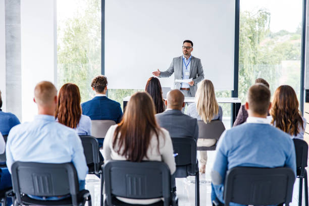 Business leader giving a speech on a seminar in board room. Male CEO standing in front of a projection screen and talking to large group of his colleagues on education event in board room. Copy space. seminar stock pictures, royalty-free photos & images