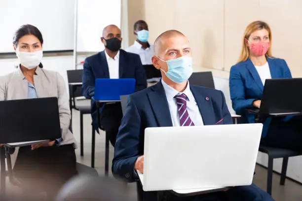 International group of business people in protective masks are working on computers in a conference room