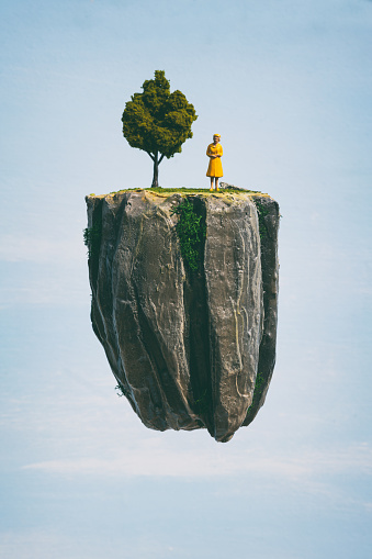 A lady dressed in a regal yellow, surely the queen and master of her own miniature world. Her world is a small floating island, drifting in the blue sky. Miniature photography.