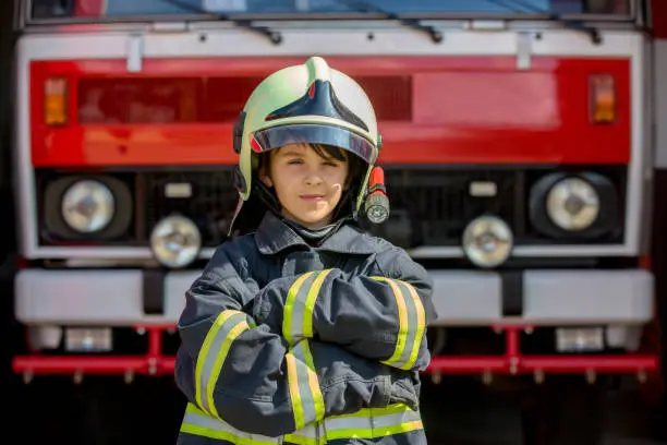 Child, cute boy, dressed in fire fighters cloths in a fire station with fire truck, Childs' dream