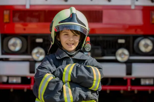 Child, cute boy, dressed in fire fighters cloths in a fire station with fire truck, Childs' dream